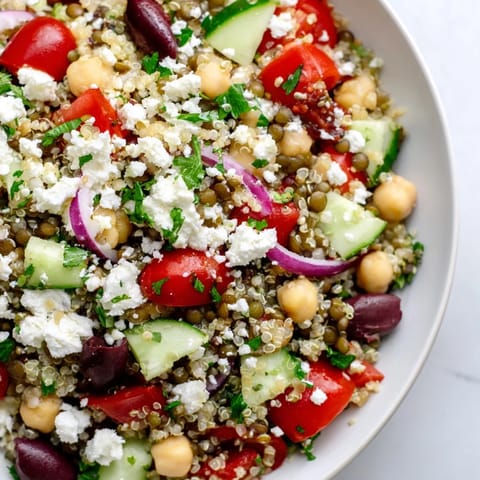 Greek Power Salad served in a rustic ceramic bowl, with crumbled feta, Kalamata olives, and diced cucumber over a bed of hearty lentils and quinoa.
