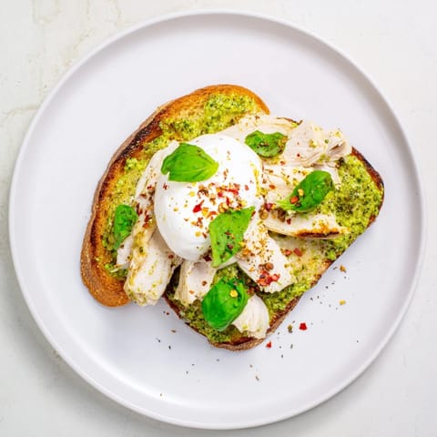 Golden, crisp sourdough slices topped with pesto, tender chicken, and creamy burrata, garnished with fresh basil leaves.