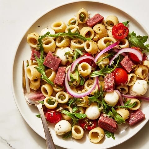 Colorful Spring Antipasto Pasta Salad served in a rustic bowl, featuring cherry tomatoes and red onion for a vibrant spring gathering side.