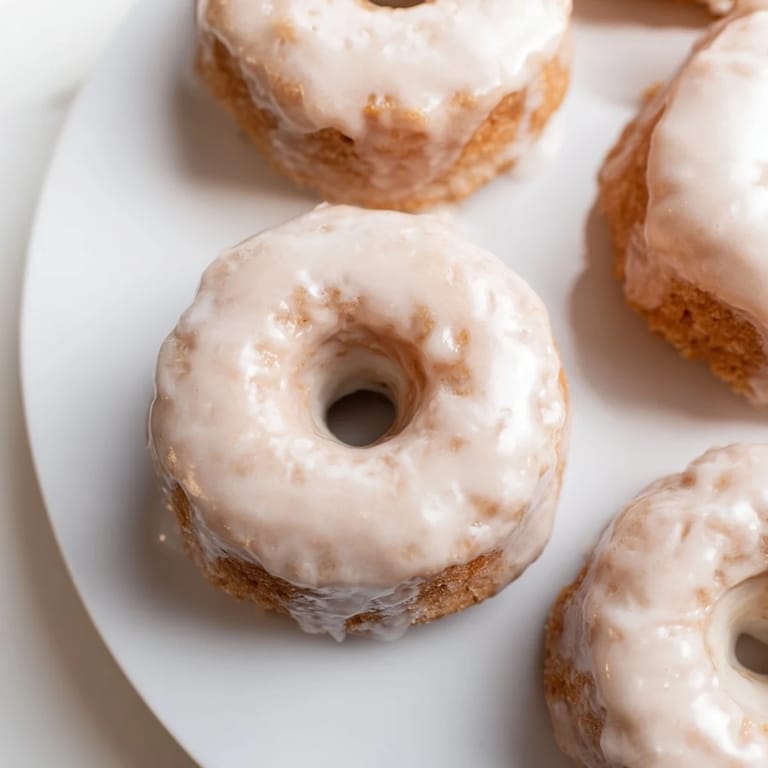 Freshly baked muffin tin donuts, glistening with a creamy vanilla glaze, ready to enjoy.