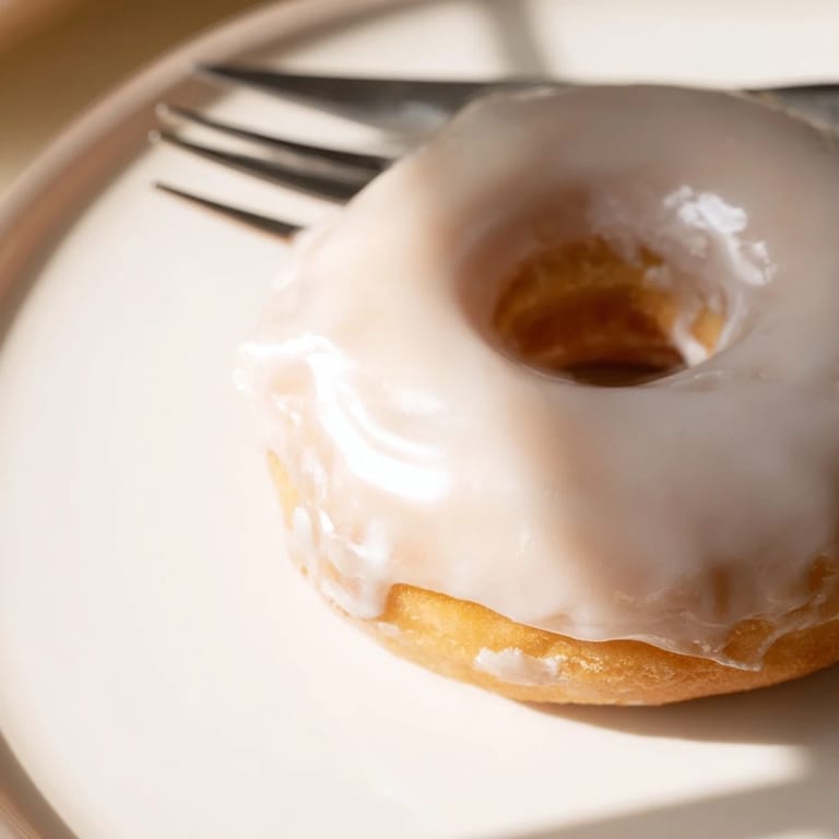 A plate of homemade yeast donuts coated in a creamy glaze, ideal for a morning treat.