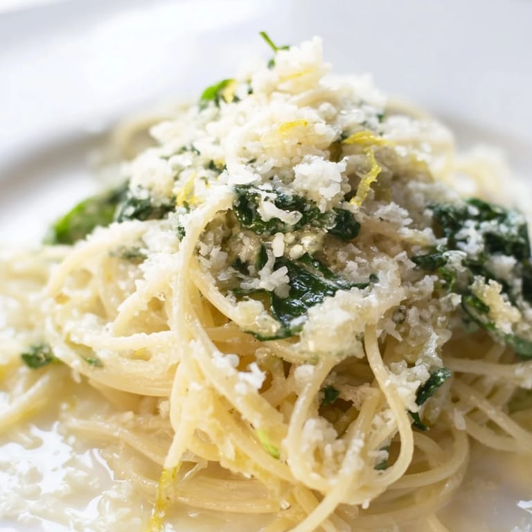 Creamy lemon spinach spaghetti served in a white bowl, garnished with extra Parmesan and a side of garlic bread.
