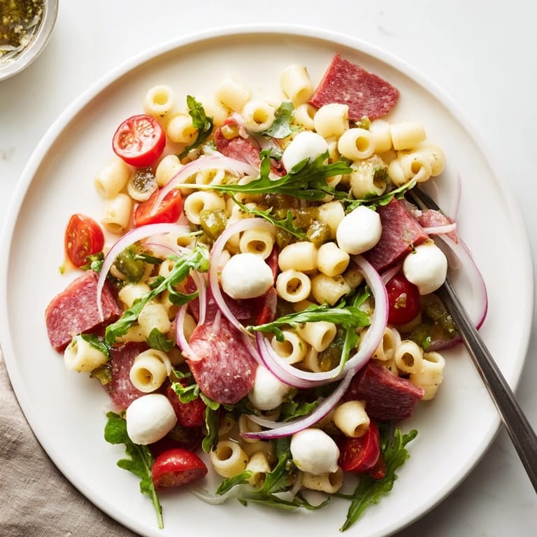 Chilled Spring Antipasto Pasta Salad with creamy mozzarella, savory salami, and crisp arugula, finished with a sprinkle of oregano and chili flakes.