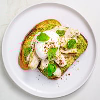Golden, crisp sourdough slices topped with pesto, tender chicken, and creamy burrata, garnished with fresh basil leaves.