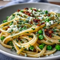 Creamy lemon butter pasta with peas and Parmesan in a skillet, garnished with fresh parsley and extra cheese.